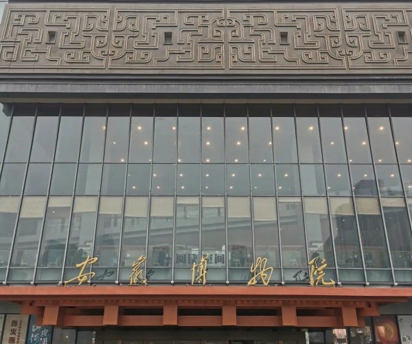 Anhui Museum,Anhui,China tour Facade of a modern building with three decorative geometric relief panels above a glass entrance; gold Chinese characters along the awning; people walking on a wet sidewalk.