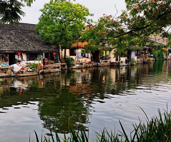 Anchang Ancient Town,Shaoxing,Chinatravel A canal lined with traditional houses, boats, and laundry drying on the shore, with green trees overhead and reflections in the water.