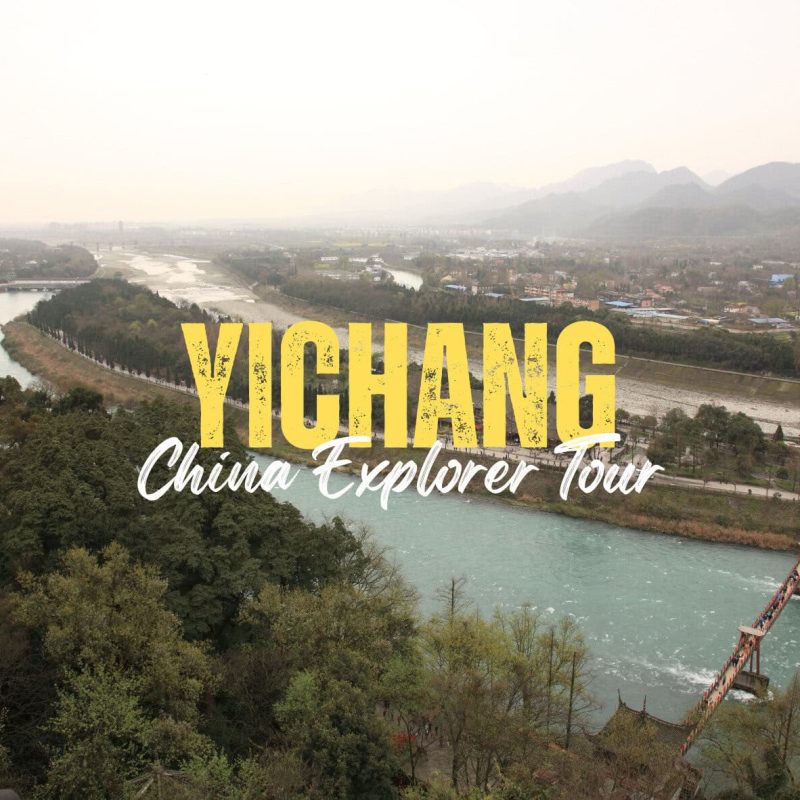 Yichang,Hunan,Chinatravel Aerial view of Yichang landscape with a river and distant mountains; large yellow 'YICHANG' and white 'China Explorer Tour' text overlay on the scene.