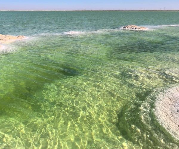 Qarhan Salt Lake,Haixi Prefecture,China tour Clear turquoise water near a sandy shore under a blue sky, with submerged rocks and rippling sunlight.