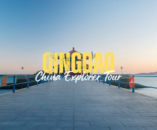 Qingdao,Shandong,China tour Promotional banner reading 'QINGDAO China Explorer Tour' on a seaside pier at sunset with blue railings and calm water in the background.