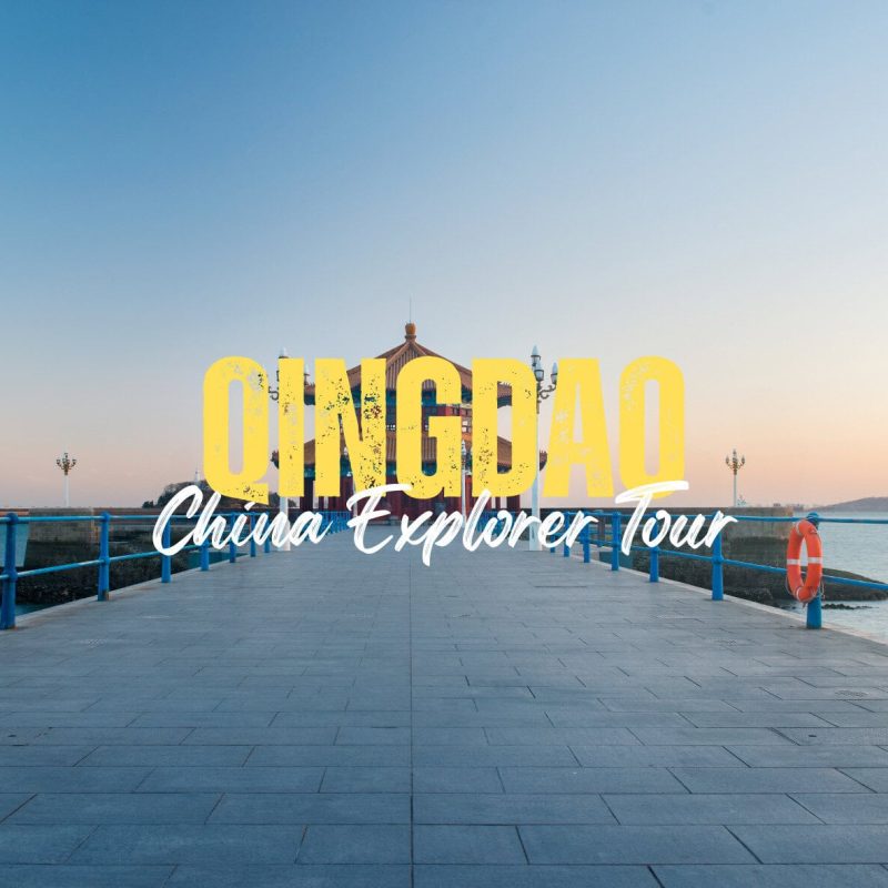 Qingdao,Shandong,China tour Promotional banner reading 'QINGDAO China Explorer Tour' on a seaside pier at sunset with blue railings and calm water in the background.