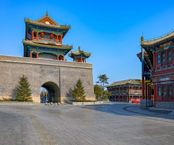Shanhaiguan,Qinhuangdao,Chinatravel Stone city gate with a multi-tiered, colorful pagoda-style tower and red lanterns against a bright blue sky.