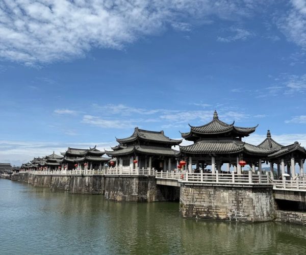Guangji Bridge,Chaozhou,Chinatravel Row of traditional Chinese pavilions on a stone walkway over calm water, with red lanterns and a blue sky above.