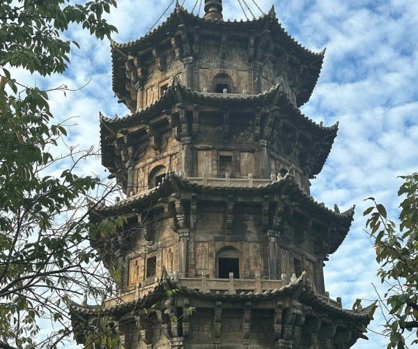 Kaiyuan Temple & West Street,Quanzhou,Chinatravel Stone multi-tier pagoda with ornate, upturned eaves rising above surrounding trees and a blue sky behind it.