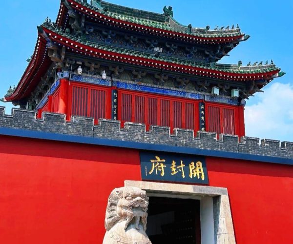 Kaifeng Mansion,Kaifeng,China tour Traditional Chinese temple gate with a ornate multi-tiered roof, red walls, and a stone guardian lion at the entrance beneath a gold plaque with Chinese characters.