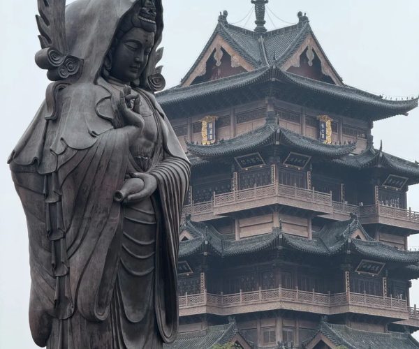 Guiyuan Buddhist Temple,Wuhan,Chinatravel Bronze statue of Guanyin with a flame-like halo beside a multi-tier Chinese pagoda temple in the background.