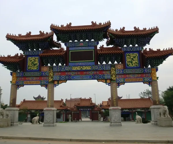 Three Kingdoms City,Suzhou,Chinatravel Colorful traditional Chinese paifang arch with ornate blue, red, and gold patterns, leading to a temple complex.
