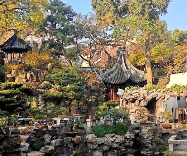Shanghai Yu Garden,Chinatour Traditional Chinese garden with rockery, pavilions, and a curved tiled roof wall in autumnal colors beneath a blue sky