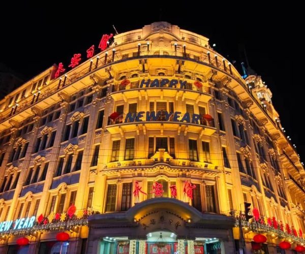 Nanjing Road,Chinatour Ornate night-time building facade lit in warm yellow lights with 'Happy New Year' banners and red lanterns outside.