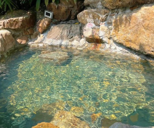 Longmen Hot Springs,Huizhou,Chinatravel Clear turquoise pool edged by large rocks and tropical plants, with sunlight shimmering on the water.