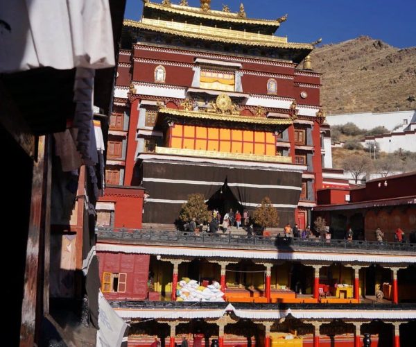 Tashilhunpo Monastery,Shigatse,China tour Tibetan Buddhist temple with red and gold ornate architecture against a hillside, visitors on the steps and courtyard in the foreground.