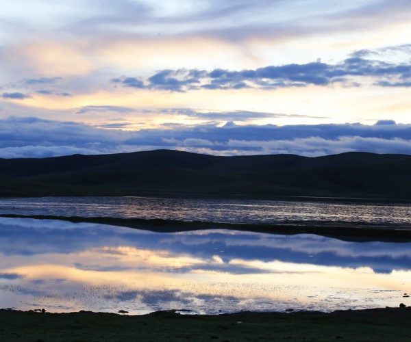 Zaling Lake & Eling Lake,Yushu,China tour Dusk over a calm lake with silhouetted hills and a pastel sunset reflected in the water's surface