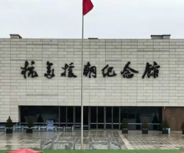 Memorial Hall of the War to Resist U.S. Aggression and Aid Korea,Dandong,China tour Facade of a memorial hall with a large Chinese inscription, a tall flagpole with a red flag, and a green platform with red decorative stars in front.