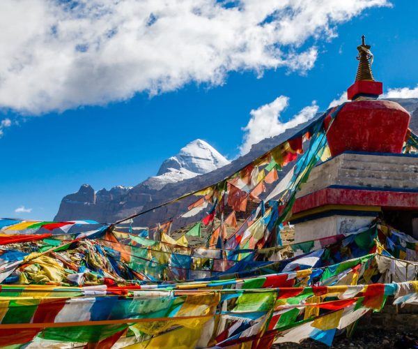 Tibet Weather,Tibet,China tour Colorful prayer flags surround a red-and-white stupa with snow-capped mountains in the blue sky.