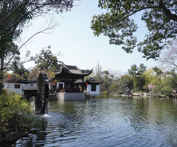 Humble Administrator’s Garden,Suzhou,Chinatravel Traditional Chinese pavilion on a lake with white walls and curved black-tiled roof, surrounded by trees.