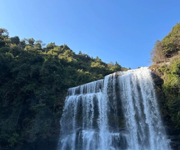Huangmanzhai Waterfall Group,Jieyang,Chinatravel Wide waterfall cascades over rock ledges into a turquoise pool, surrounded by green forest under a clear blue sky.
