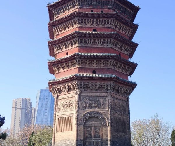 Wenfeng Pagoda,Anyang,Chinatravel Multi-tiered red-brick Chinese pagoda in a park, with ornate eaves and a carved stone base, blue sky above and modern buildings in the distance.