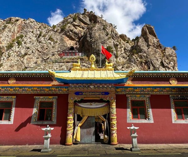 Princess Wencheng Temple/Monument,Yushu,China tour Colorful Buddhist temple with a gold-tiled roof and red walls, set against a rocky mountain backdrop and blue sky, flag flying above.