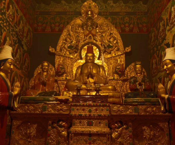 Changzhu Temple,Shannan,China tour Gilded Buddhist altar with central seated statue in prayer pose, flanked by ornate figures in a richly decorated temple chamber.