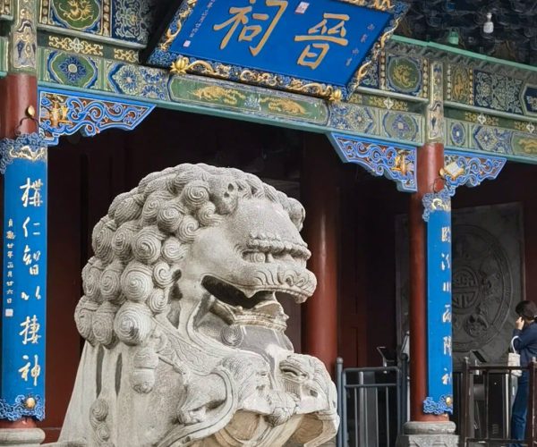 Jinci Temple,Taiyuan,Chinatravel Stone Chinese guardian lion statue at the temple entrance, with a blue plaque and ornate painted eaves above in blue, green, and gold.