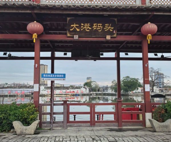 Nanxi Water Town,Jieyang,Chinatravel Traditional Chinese pavilion by a canal with red lanterns, flags, and a sign reading 大港码头 overlooking boats and water.