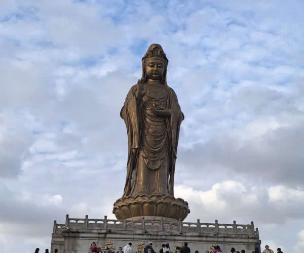 Putuo Mountain,Zhoushan,Chinatravel Bronze statue of a standing Buddhist deity with one hand raised, on a lotus pedestal amid visiting crowds.