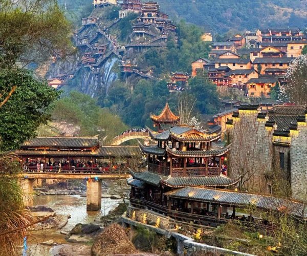 Wangxian Valley,Shangrao,Chinatrip hillside town with traditional Chinese pagodas on a mountain, a curved bridge over a river, and a tiled village in the valley