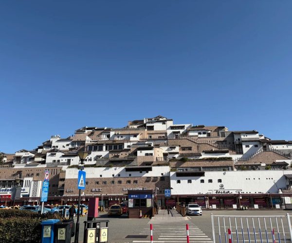 Zhujiajian Island ,Zhoushan,Chinatravel White tiered houses with brown-tiled roofs stacked on a hillside under a clear blue sky; shops and parked cars at street level.