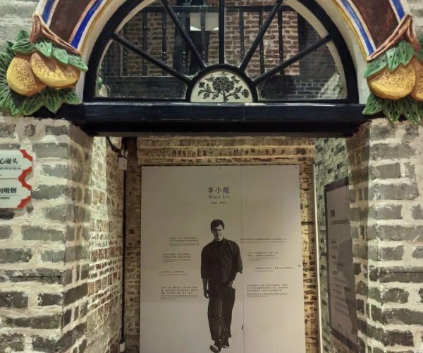 Bruce Lee Ancestral Home,Foshan,Chinatravel Decorative archway with blue and gold trim above a brick passage, leading to a display panel featuring Bruce Lee posters and Chinese text.