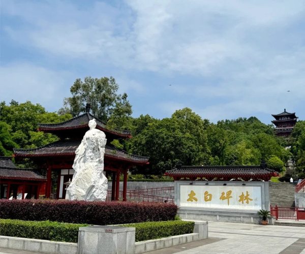 Li Bai's Former Residence,Mianyang,Chinatravel White stone statue in a Chinese temple courtyard with red pavilions behind, and a stone sign with gold Chinese characters under a blue sky.