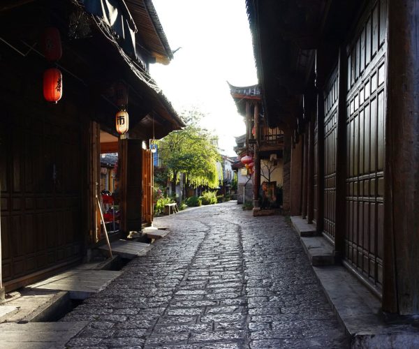 Shuhe Ancient Town,Lijiang,Chinatravel Narrow cobblestone alley between dark wooden shopfronts with hanging red lanterns in a traditional Asian town.