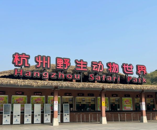Hangzhou Safari Park,Hangzhou,Chinatravel Hangzhou Safari Park entrance sign with large red Chinese characters and 'Hangzhou Safari Park' in English, under a thatched roof with ticket kiosks below.