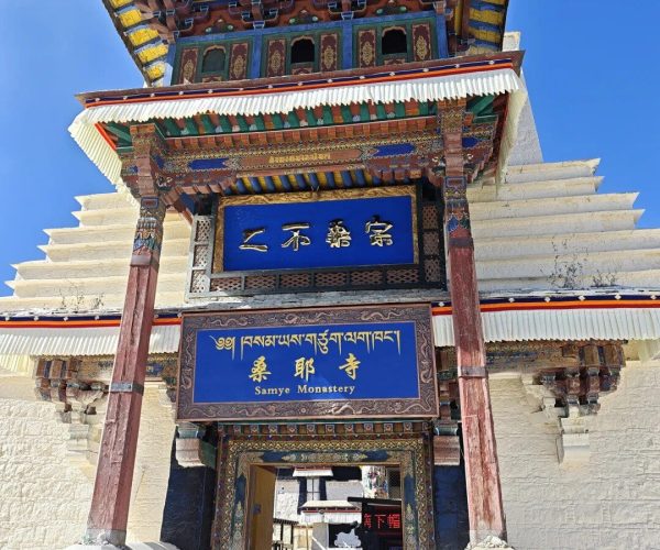 Samye Monastery,Shannan,China tour Entrance gate to Samye Monastery with colorful Tibetan architecture against a clear blue sky, blue signboards visible.