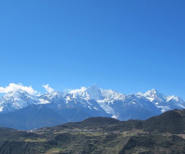 Meili Snow Mountain,Shangri-La,Chinatravel Snow-capped mountain range under a clear blue sky with a green valley and small village in the foreground.