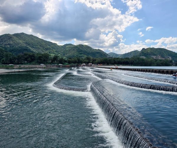 Nanxi River,Wenzhou,Chinatravel Terraced river with cascading steps, people along the bank, and green mountains under a partly cloudy sky.