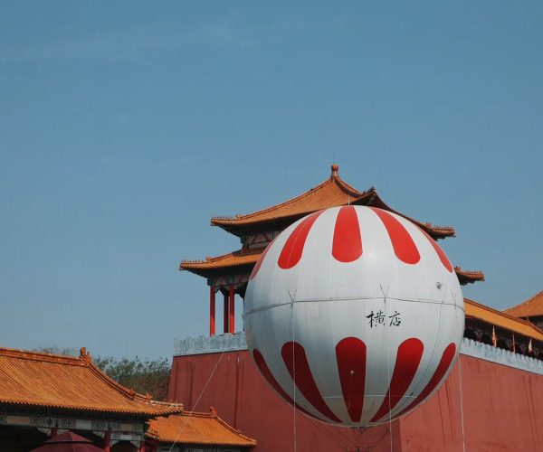 Hengdian World Studios,Zhejiang,Chinatravel Large white balloon with red teardrop panels anchored in front of traditional Chinese temple buildings with orange tiled roofs.