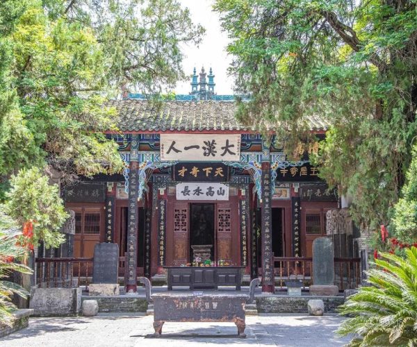 Wuhou Shrine, Chengdu, Chinatravel, Temple gate with ornate wooden pillars and Chinese signage, framed by green trees.