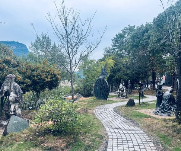China Wuyi Tea Expo Park,Nanping,Chinatravel Stone statues along a winding stone path in a garden, with trees and distant hills in the background.