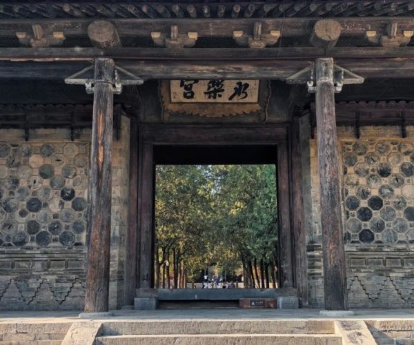 Yongle Palace,Yuncheng,Chinatravel Stone steps lead up to a traditional Chinese temple gate with wooden pillars and a plaque, opening to a tree-filled courtyard.