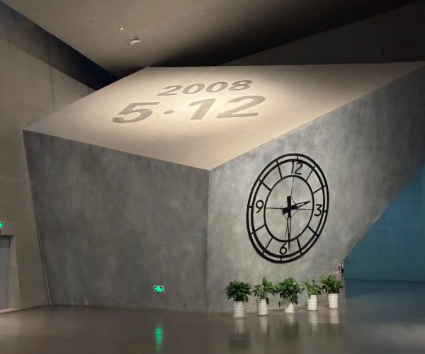Jiangyou Earthquake Museum,Mianyang,Chinatravel Interior sculpture: a tilted concrete cube with '2008 5.12' inscribed on its top and a large clock graphic on the side, plants at the base.