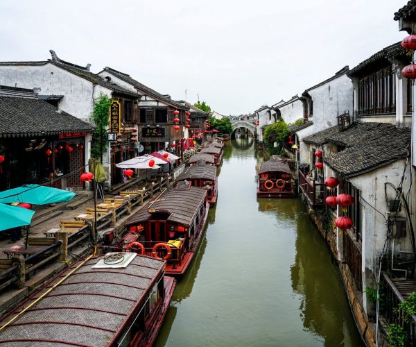 Jiangsu Weather,Jiangsu,China tour Narrow canal in a traditional Chinese town with wooden boats and red lanterns along white-washed buildings.