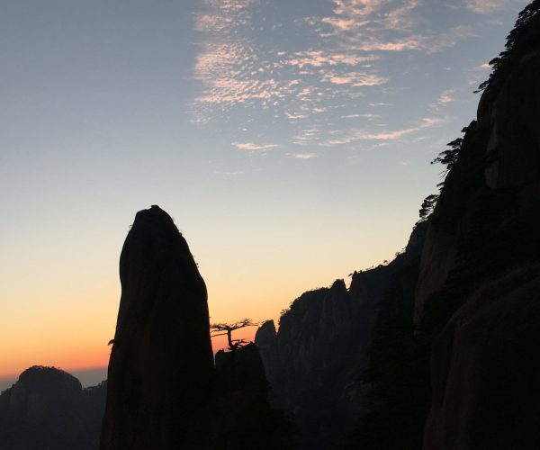 Jiangxi Weather,Jiangxi,China tour Silhouetted jagged rock spires at sunset, with an orange horizon and a pale blue sky above.