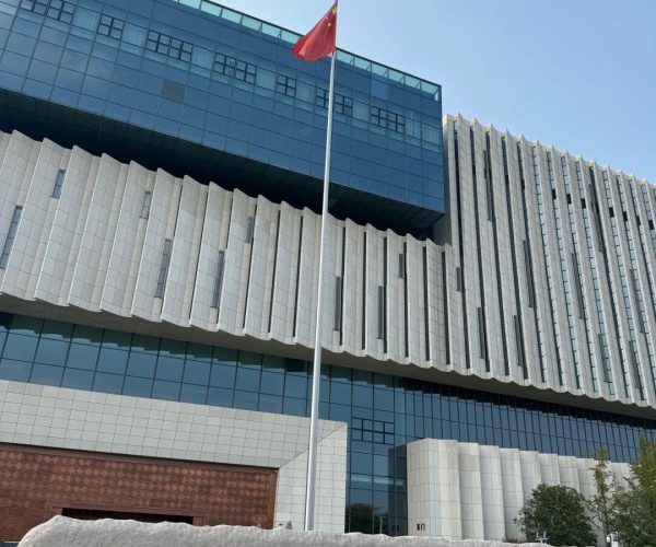 Jiangxi Provincial Museum,Nanchang,China tour Flagpole with a red Chinese flag in front of a modern glass-and-stone building, with gold inscription on a stone wall in the foreground