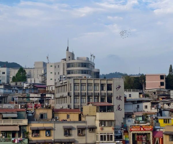 Shapowei,Xiamen,Chinatravel Dense cityscape along a river with colorful storefronts and mid-rise buildings under a blue sky with scattered clouds and birds overhead UX.