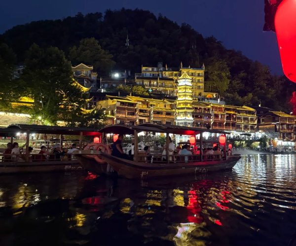 Cruising the Tuo River,Fenghuang,Chinatravel Nighttime riverside scene with illuminated traditional buildings, red lanterns, and boats on calm water with reflections in a dark sky.