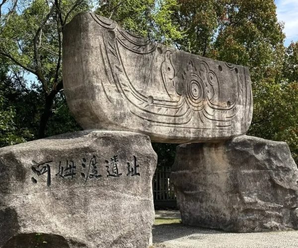 Hemudu Ancient Site,Ningbo,Chinatravel Large stone monument supported by two boulders, with flowing carved patterns and a Chinese inscription on the front.