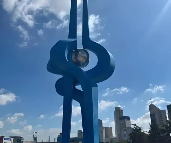 Quancheng Square,Jinan,China tour Blue abstract sculpture with intertwined loops around a glass sphere, set in a city plaza with skyscrapers in the background.
