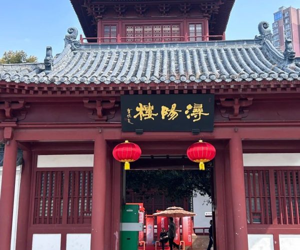 Xunyang Towe,Jiujiang,China tour Traditional red temple-style gate with gray tiled roof, a gold-character sign, and two red lanterns at the entrance.
