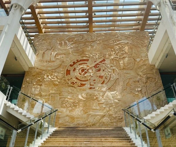 Hainan Museum,Haikou,Chinatravel Grand marble staircase in a modern atrium with a large beige carved wall relief featuring a circular central motif and surrounding scenes of landscape and architecture.